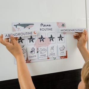 Może przedstawiać: Schemat rutynowy dla dzieci ze słowami "Meine ROUTINE", "ABENDROUTINE" i "MORGENROUTINE". Schemat zawiera ilustracje wieloryba, gwiazd i ikon dla zadań takich jak korzystanie z toalety i mycie rąk.
