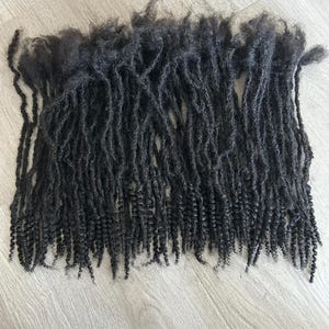 May include: A bundle of black human hair dreadlocks. The dreadlocks are long and thick, and they are arranged in a loose, flowing style.