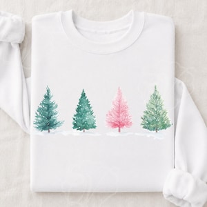 Könnte beinhalten: Ein weißes Langarm-Sweatshirt mit Rundhalsausschnitt und einer Aquarell-Grafik von vier Tannenbäumen in einer Reihe. Die Bäume sind in den Farben Dunkelgrün, Mittelgrün, Rosa und Hellgrün gehalten und stehen auf einem verschneiten weißen Untergrund.