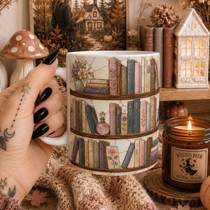 Könnte beinhalten: Ein weißer Keramikbecher mit einer umlaufenden Illustration von drei Holzregalen, die mit bunten Büchern, kleinen Topfblumen und einer Glasparfümflasche gefüllt sind. Das Design zeigt detaillierte Buchrücken und florale Akzente.