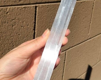 May include: A white selenite wand with a smooth, polished surface. The wand is approximately 15 cm long and has a rectangular shape.
