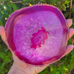 May include: A large, pink agate slice with a white and pink crystal pattern. The agate is translucent and has a smooth, polished surface.