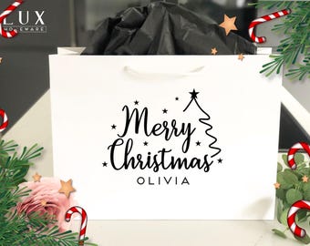 Pode incluir: Saco de presente branco com a frase "Merry Christmas OLIVIA" em escrita preta, com um desenho de árvore de Natal. Decorado com bengalas doces, estrelas e vegetação, evocando um ambiente festivo.