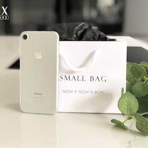 May include: A white gift bag with black text that reads "SMALL BAG 16CM X 12CM X 8CM". A silver iPhone is in the foreground.