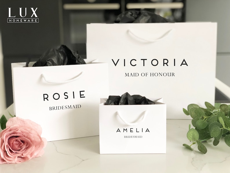 May include: Three white gift bags with black text. The bags are labeled "Rosie Bridesmaid", "Amelia Bridesmaid", and "Victoria Maid of Honour".