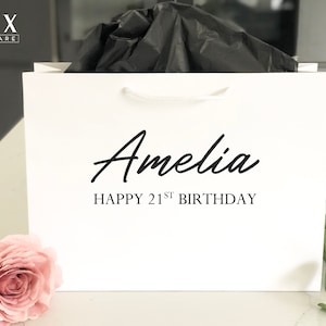 May include: White gift bag with black handles and the text "Amelia Happy 21st Birthday" printed on the front.