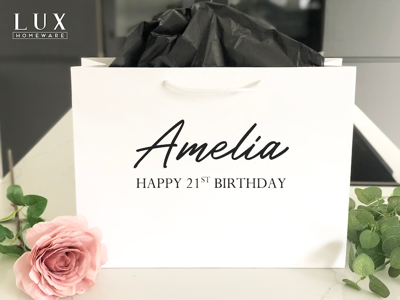 May include: White gift bag with black handles and the text "Amelia Happy 21st Birthday" printed on the front.