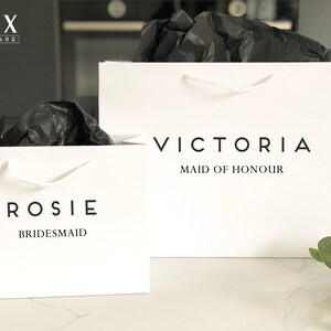 May include: Two white gift bags with black text. The bag on the left says "Rosie Bridesmaid" and the bag on the right says "Victoria Maid of Honour".