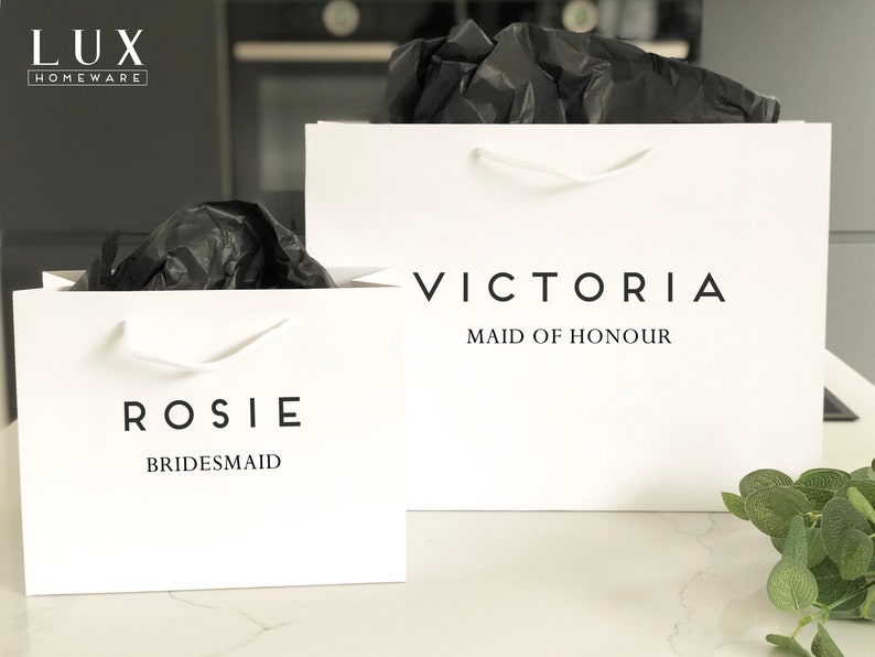 May include: Two white gift bags with black text. The bag on the left says "Rosie Bridesmaid" and the bag on the right says "Victoria Maid of Honour".