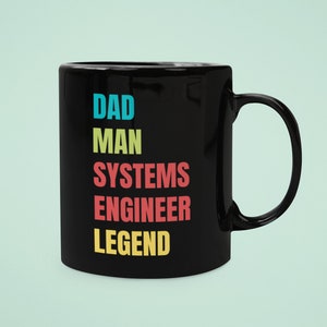 May include: Black ceramic coffee mug with the text "DAD MAN SYSTEMS ENGINEER LEGEND" in colorful letters.