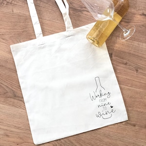 Könnte beinhalten: Weiße Stofftasche mit schwarzem Text, der "Working from nine to wine" mit einem kleinen Herz und einer Zeichnung einer Weinflasche lautet.