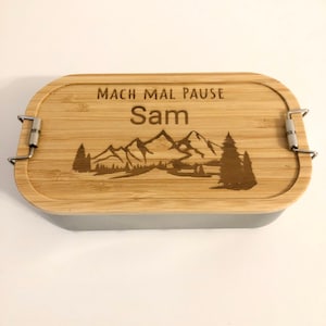 Könnte beinhalten: Eine graue und braune Lunchbox mit einem Holzdeckel. Der Deckel hat eine Bergszene und den Text "Mach mal Pause Sam" eingraviert.