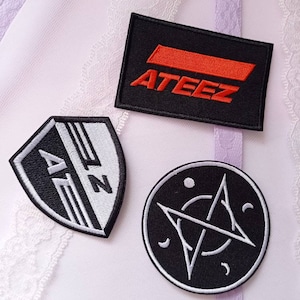 以下が含まれることがあります： 3つの刺繍ワッペン：オレンジ色の「ATEEZ」の文字が入った黒い長方形のワッペン、AZの文字と水平線が入った盾形の白黒ワッペン、そして白い星と三日月のデザインが施された円形の黒いワッペン。