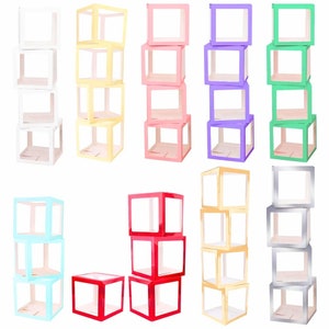 Op de afbeelding: Set van tien doorzichtige plastic dozen in verschillende kleuren, waaronder wit, geel, roze, paars, groen, rood, blauw, zilver en goud. Elke doos is gemaakt van doorzichtig plastic met een gekleurde rand en is gestapeld in een toren van drie dozen.