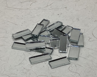 May include: A pile of small, rectangular mirror tiles. The tiles are silver and have a reflective surface.
