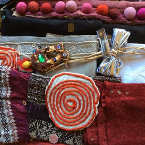 May include: A collection of colorful fabric scraps with various textures and patterns, including a red and white spiral design, a brown fabric with a green and gold embellishment, and a silver ribbon with a bow.