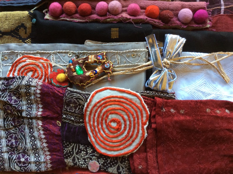 May include: A collection of colorful fabric scraps with various textures and patterns, including a red and white spiral design, a brown fabric with a green and gold embellishment, and a silver ribbon with a bow.
