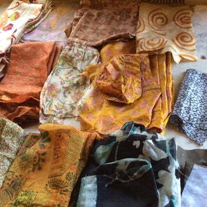May include: Assortment of fabric scraps in various colors and patterns, including floral, paisley, and geometric designs. The fabrics are mostly in shades of orange, brown, and black.