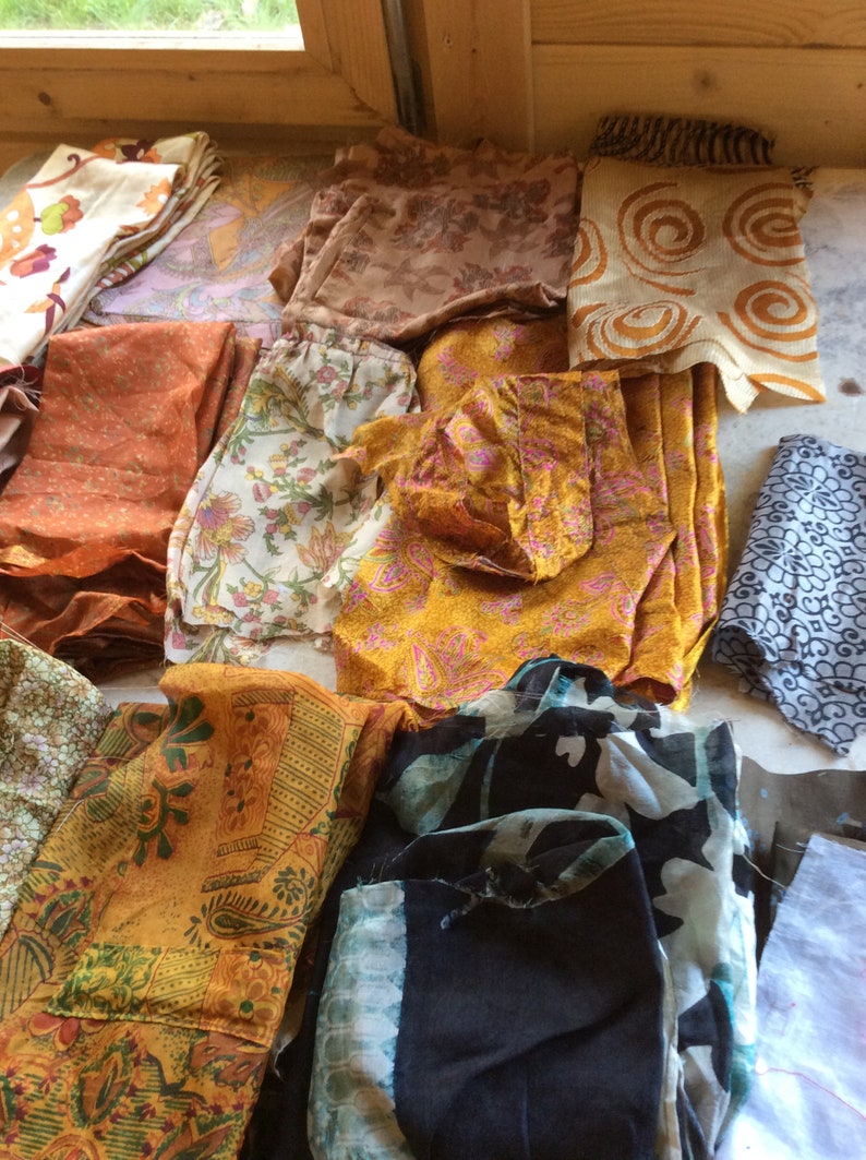 May include: Assortment of fabric scraps in various colors and patterns, including floral, paisley, and geometric designs. The fabrics are mostly in shades of orange, brown, and black.