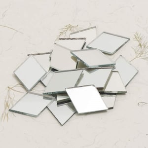 May include: A pile of small, diamond-shaped mirror tiles. Each tile has a reflective surface and a beveled edge. The tiles are scattered on a light-coloured surface, creating a mosaic effect. Suitable for craft projects or home decor.