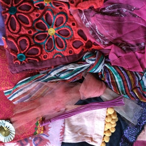 May include: A collection of fabric scraps in various shades of pink, red, and purple. The fabrics are a mix of textures, including lace, tulle, and patterned cotton. Some of the fabrics have embroidered details.