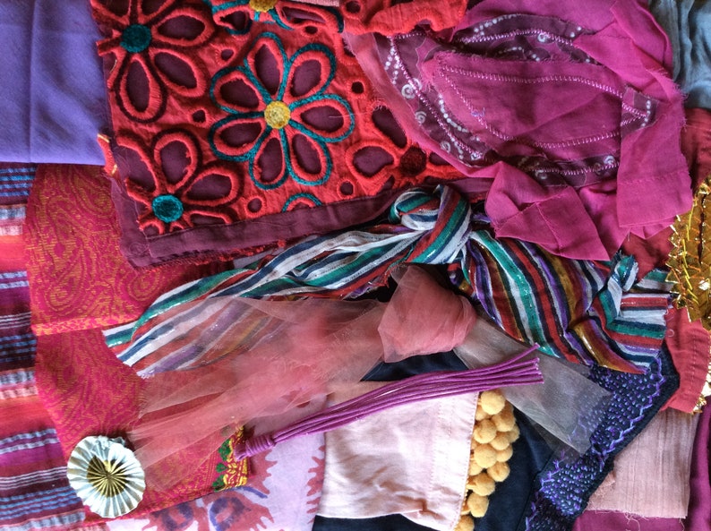 May include: A collection of fabric scraps in various shades of pink, red, and purple. The fabrics are a mix of textures, including lace, tulle, and patterned cotton. Some of the fabrics have embroidered details.