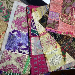 May include: A patchwork of fabric squares sewn together to create a larger piece. The fabric squares are in various colors, including pink, purple, green, and gold. Each square features intricate embroidery and beading.