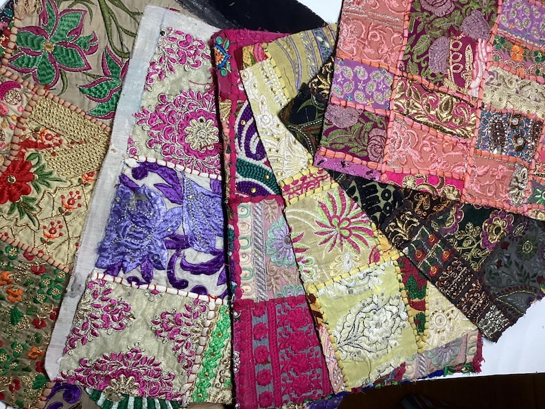 May include: A patchwork of fabric squares sewn together to create a larger piece. The fabric squares are in various colors, including pink, purple, green, and gold. Each square features intricate embroidery and beading.
