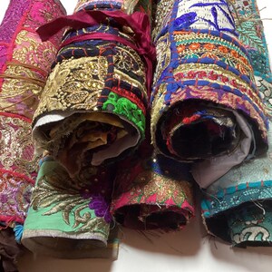May include: Five colorful fabric rolls with intricate embroidery and embellishments. The rolls are made of different fabrics, including velvet, silk, and cotton. The fabrics are all in various shades of pink, blue, green, and gold.