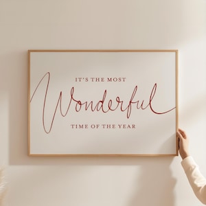 May include: A framed rectangular print with the text "IT'S THE MOST Wonderful TIME OF THE YEAR" in red script on a white background. The frame is a light brown color.