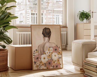 May include: A framed art print featuring a woman's back with a floral design. The artwork showcases a woman with her hair up, surrounded by pink, yellow, and white flowers. The print is displayed in a light-colored wooden frame, leaning against a box in a well-lit room.