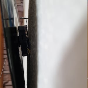May include: Close-up of a black clock mechanism mounted on a wall. The clock mechanism has a silver hand and a black metal frame.