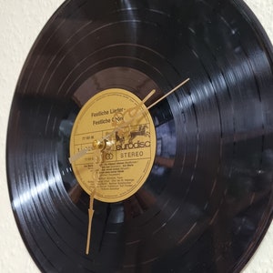 Könnte beinhalten: Eine schwarze Schallplattenuhr mit goldenen Zeigern und einem goldenen Etikett. Das Etikett trägt den Text "Festliche Lieder - Festliche Chöre" und "eurodisc STEREO".