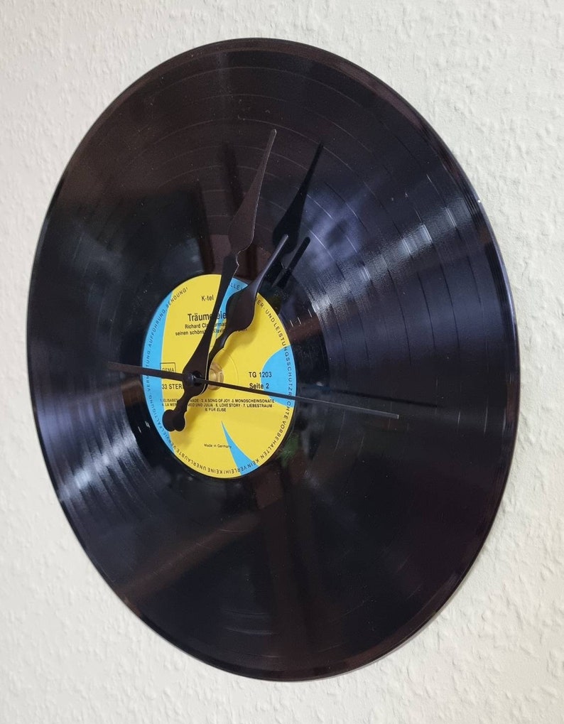 May include: A black vinyl record clock with black hands. The record label is yellow with blue text that reads "Traumreise" and "Seite 2".