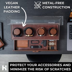 May include: A brown leather watch and accessory organiser with a clear lid. The organiser has a drawer with compartments for wallets, keys, and other small items. The text on the image says "VEGAN LEATHER PADDING" and "METAL-FREE CONSTRUCTION."