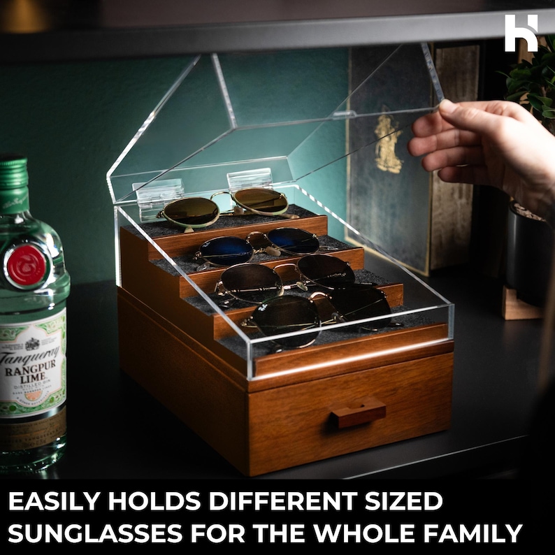 May include: A wooden sunglasses storage organizer with a clear acrylic hinged lid and a tiered interior featuring grey felt lining. The box includes a bottom drawer with a wooden handle and holds four pairs of sunglasses. Text reads: EASILY HOLDS DIFFERENT SIZED SUNGLASSES FOR THE WHOLE FAMILY.