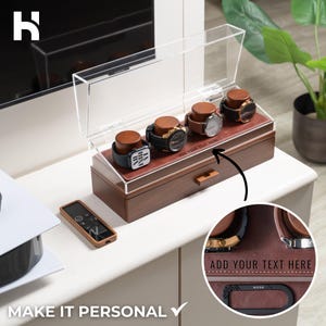 May include: A wooden watch display case with a clear acrylic lid, holding four watches with brown leather straps. The case has a brown leather interior and a small drawer. Text on the case reads "ADD YOUR TEXT HERE" and "MAKE IT PERSONAL".