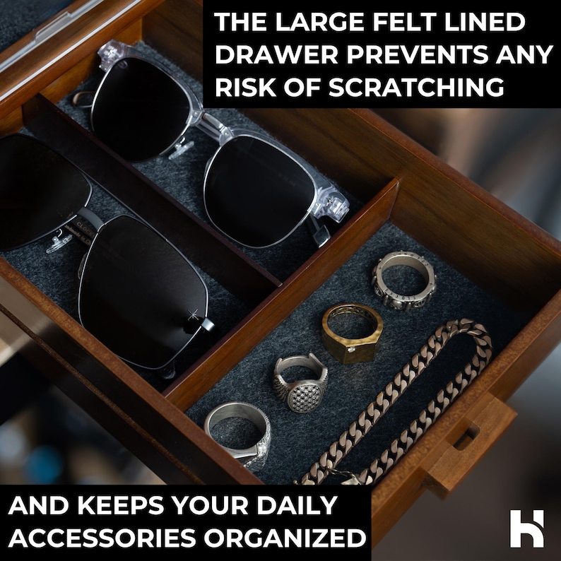May include: A wooden storage drawer with dark gray felt lining containing two pairs of sunglasses, four rings, and a metal chain link bracelet. Text reads: THE LARGE FELT LINED DRAWER PREVENTS ANY RISK OF SCRATCHING AND KEEPS YOUR DAILY ACCESSORIES ORGANIZED.