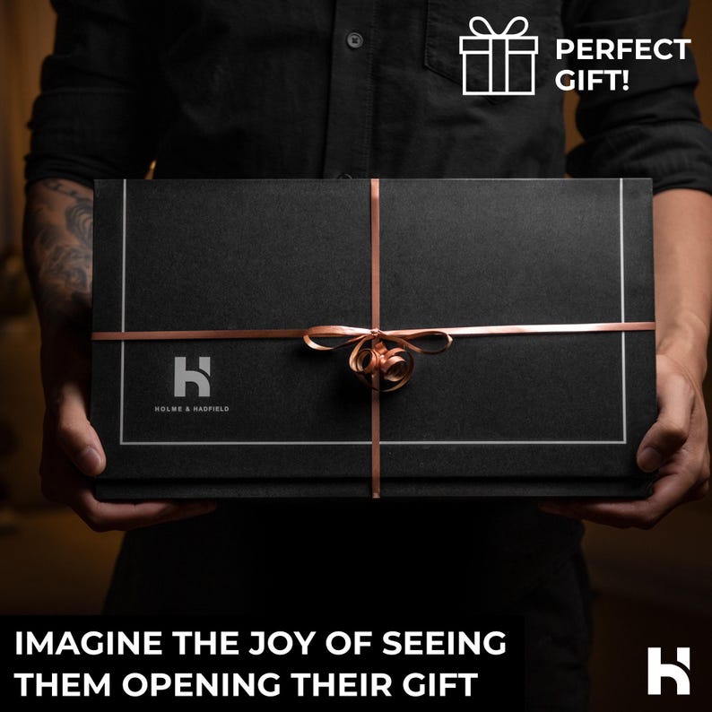 May include: A rectangular black gift box featuring a thin copper ribbon tied in a bow at the center. The box displays the white text HOLME & HADFIELD with a logo, a white gift icon with the text PERFECT GIFT!, and the text IMAGINE THE JOY OF SEEING THEM OPENING THEIR GIFT.