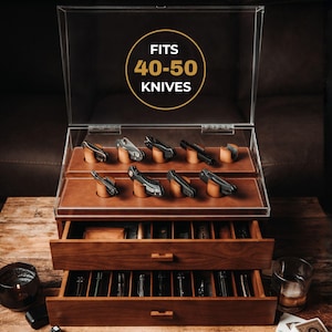 Può includere: Un cofanetto portacoltelli in legno con due cassetti estraibili e un coperchio superiore in acrilico trasparente. Il coperchio presenta una grafica circolare con il testo FITS 40-50 KNIVES. L'interno è rivestito in similpelle marrone.