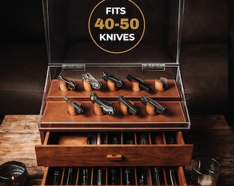 May include: A wooden knife storage chest with two pull-out drawers and a clear acrylic top lid. The lid features a circular graphic with the text FITS 40-50 KNIVES. The interior has brown leather-like lining with individual wooden knife holders.