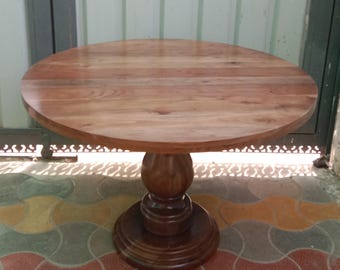 May include: A round wooden table with a pedestal base. The table top is made of light brown wood and the base is a darker brown wood.