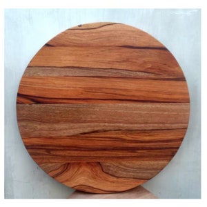Puede incluir: Una tabla de cortar redonda de madera con un acabado de madera natural. La tabla tiene un color marr&oacute;n intenso con vetas marrones m&aacute;s oscuras en toda la veta.