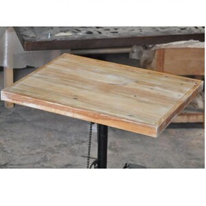 Peut inclure: Un plateau de table en bois clair avec une finition légèrement vieillie. Le plateau de table est rectangulaire et a un bord légèrement arrondi. Le plateau de table est soutenu par une base en métal noir.
