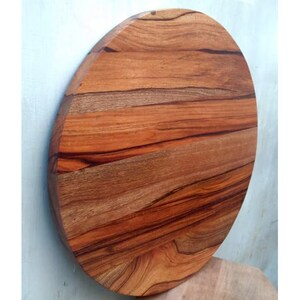 Puede incluir: Una tabla de cortar redonda de madera con un acabado de madera natural. La tabla tiene un color marr&oacute;n intenso con vetas marrones m&aacute;s oscuras en toda la veta. La tabla tiene un di&aacute;metro de aproximadamente 30 cm.