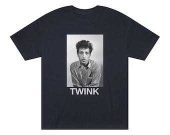May include: Navy blue t-shirt featuring a black and white portrait of a man with the word "TWINK" printed in white below the image. The t-shirt has short sleeves and a crew neck.