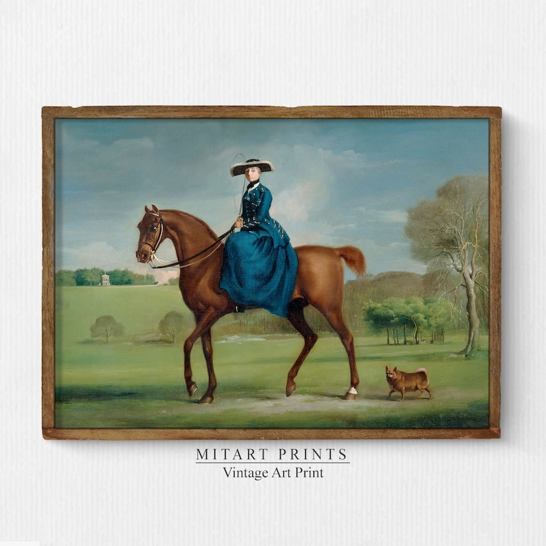 May include: A vintage painting of a woman in a blue dress riding a brown horse in a green field. A small brown dog is walking in the background. The painting is framed in a brown wooden frame. MITART PRINTS Vintage Art Print