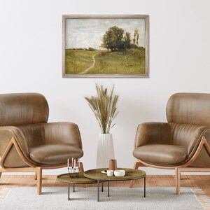 May include: Two brown leather armchairs with wooden frames, facing each other in a living room setting. A framed landscape painting hangs on the wall behind the chairs. A vase with dried wheat stalks sits on a coffee table between the chairs.