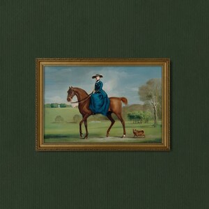 May include: A framed oil painting depicting a woman in a blue dress riding a brown horse through a green field. A small brown dog is walking behind the horse.