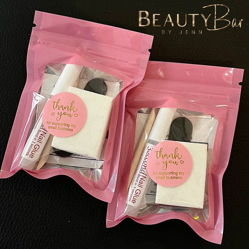May include: Two pink zippered pouches with clear windows, each containing a small bottle of nail glue, a small white square, a black nail file, and a thank you sticker that says "thank you for supporting my small business".